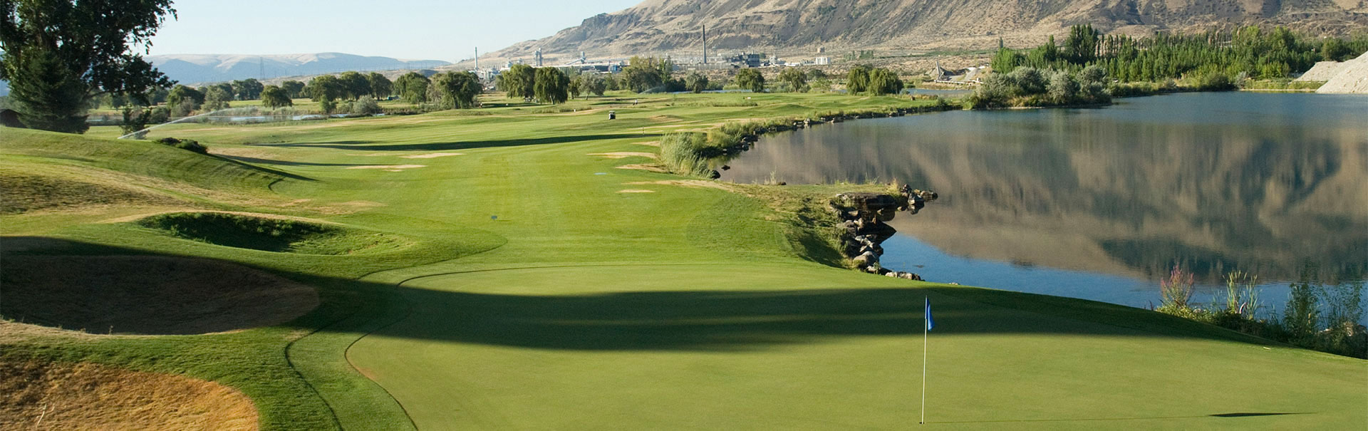 Golf course with green fairway alongside a calm lake reflecting distant hills.