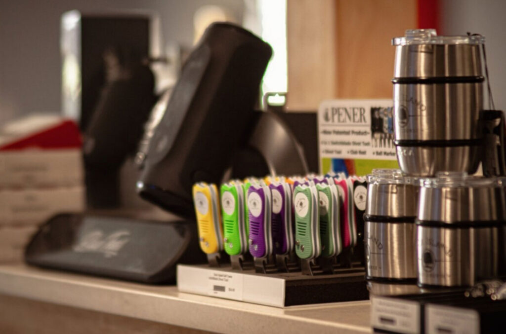 Close-up of a countertop display featuring shiny steel cups stacked on the right and colorful electronic devices in yellow, purple, and green on a stand.