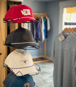 Caps on a wire rack: red, black, white, and blue, each with "Rock Island" logo. A light blue shirt with a small pattern hangs on a rack in the background.