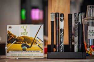 Display of golf club grips next to a sign reading "Get a Grip" promoting regripping services.