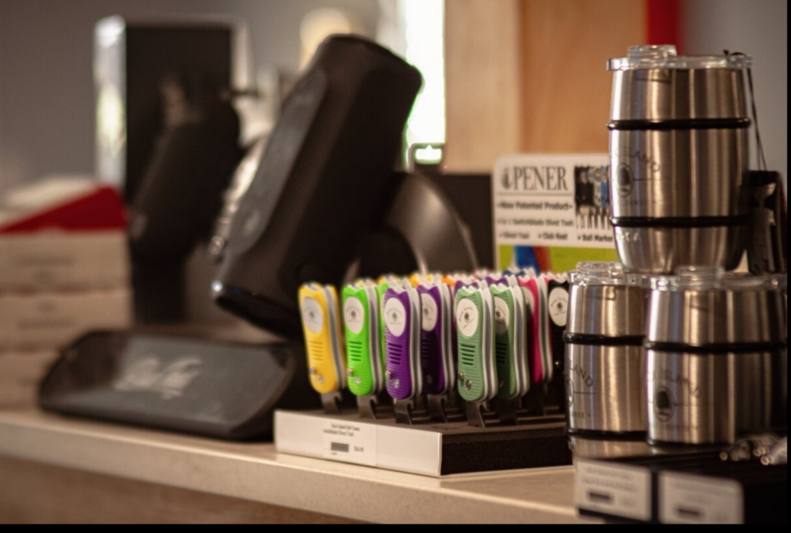 Close-up of a countertop display featuring shiny steel cups stacked on the right and colorful electronic devices in yellow, purple, and green on a stand.