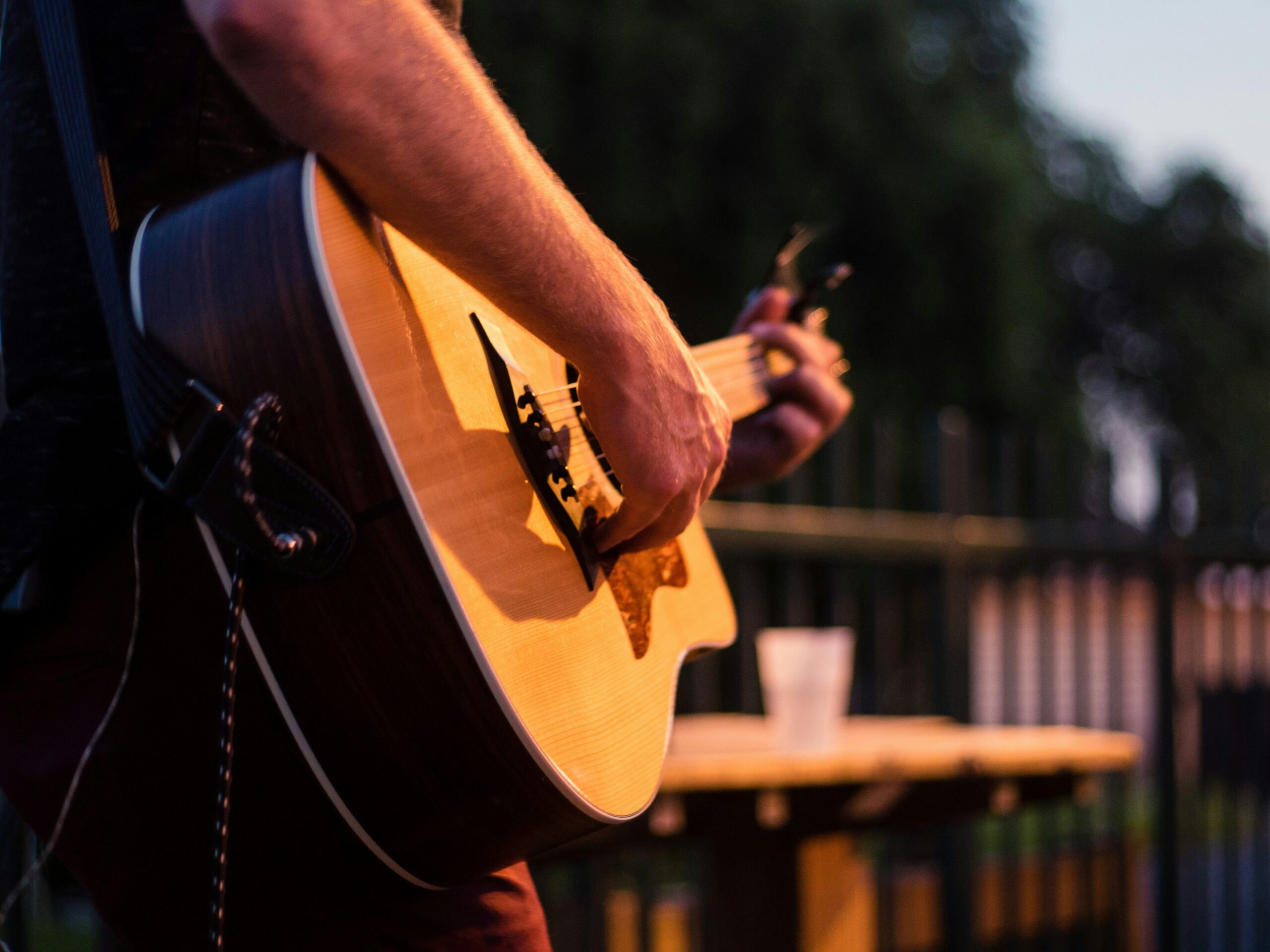 Man strumming an acoustic guitar outdoors at dusk.