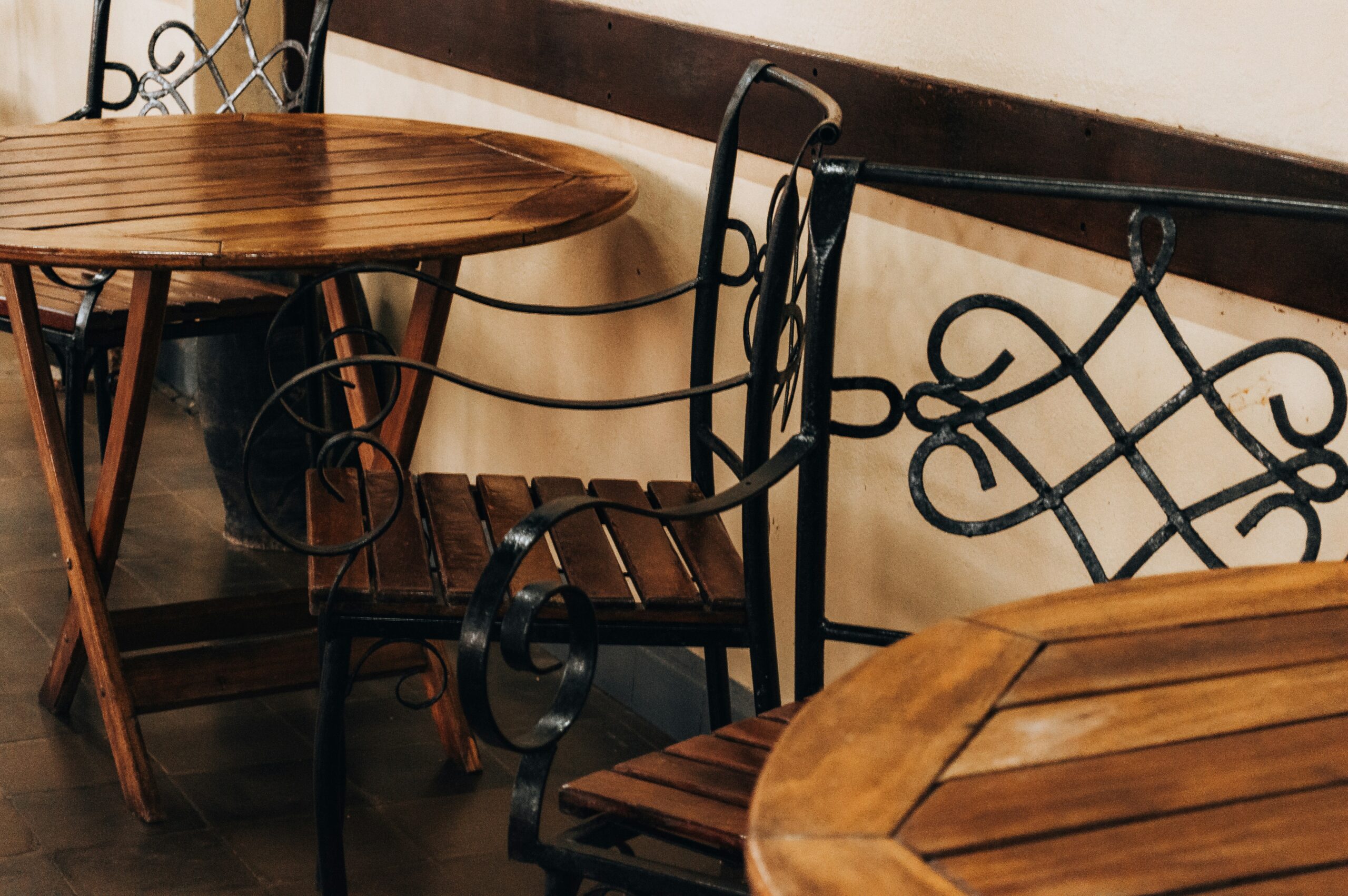 Wooden chairs with black wrought iron details are arranged around round wooden tables.