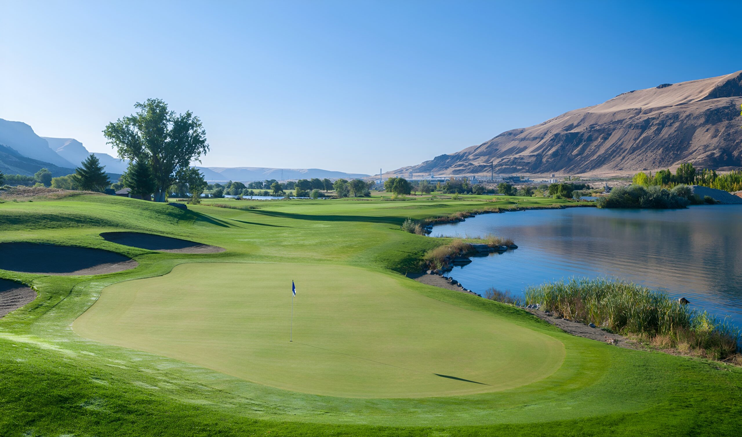 Golf course with green fairway alongside a calm lake reflecting distant hills.